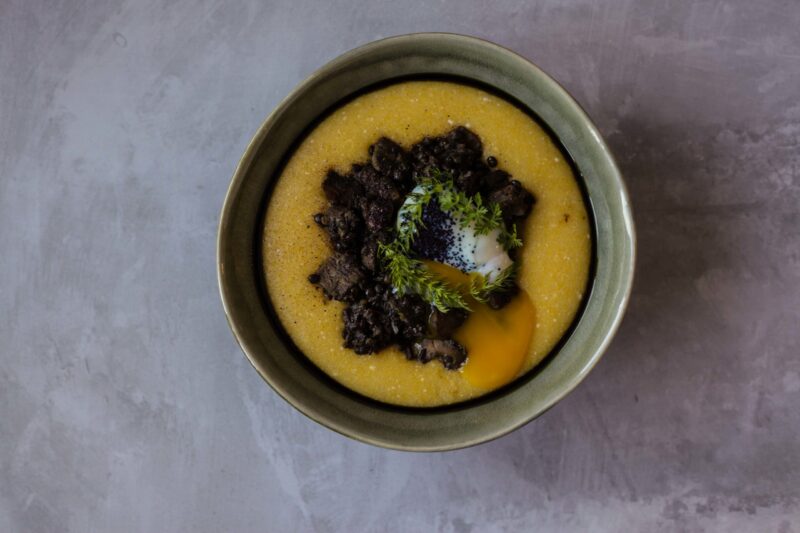 Tabletop image of mushrooms, lentils, cheesy polenta and poached egg on a grey background